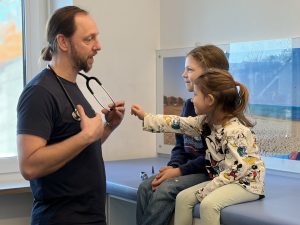 Arzt mit Stethoskop untersucht zwei Kinder