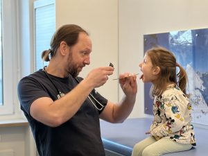 Arzt untersucht Mädchen mit Zungenspatel im Behandlungszimmer