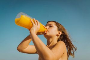 Kind trinkt Orangensaft aus großer Flasche